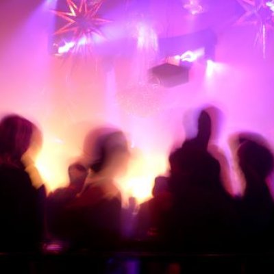 A Silhouette of people in a nightclub surrounded by pink and purple flashing lights